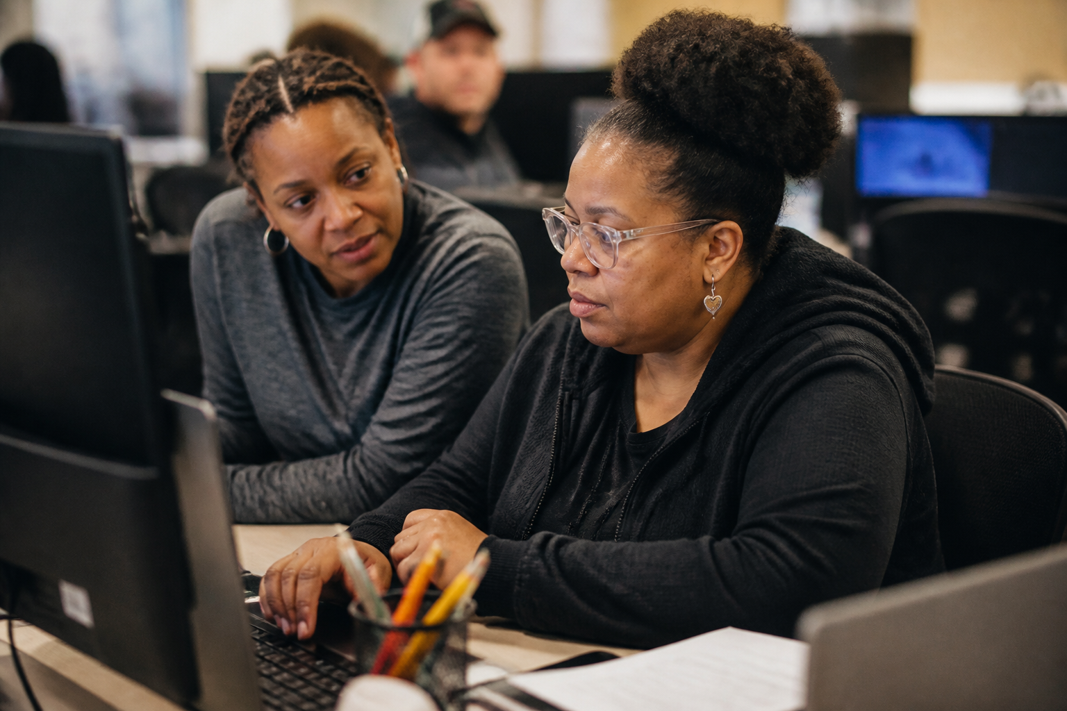 Member practices office skills at a computer with a staff mentor beside them in the clubhouse.