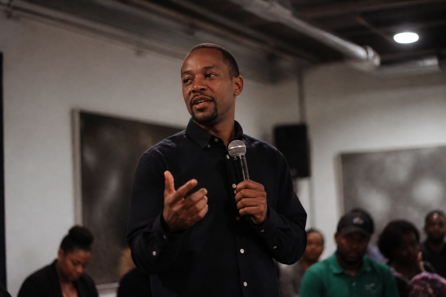 Chas Moore speaks at a community gathering in Austin with Austin Justice Coalition signage behind him.